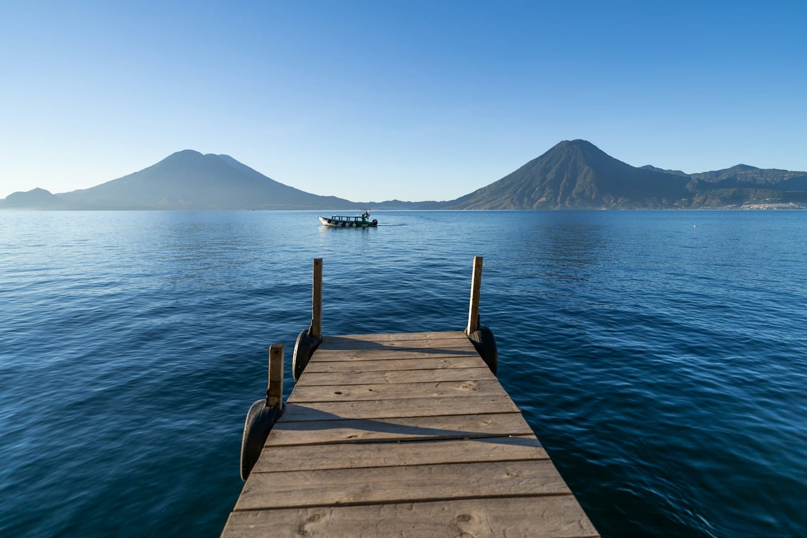 A wooden dock on Lake Atitlán with a boat and two volcanoes on the far shore