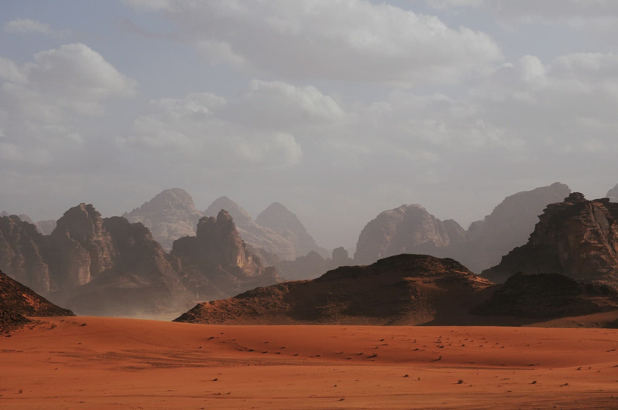 Red sand and rock mountains in the Wadi Rum desert under clouds