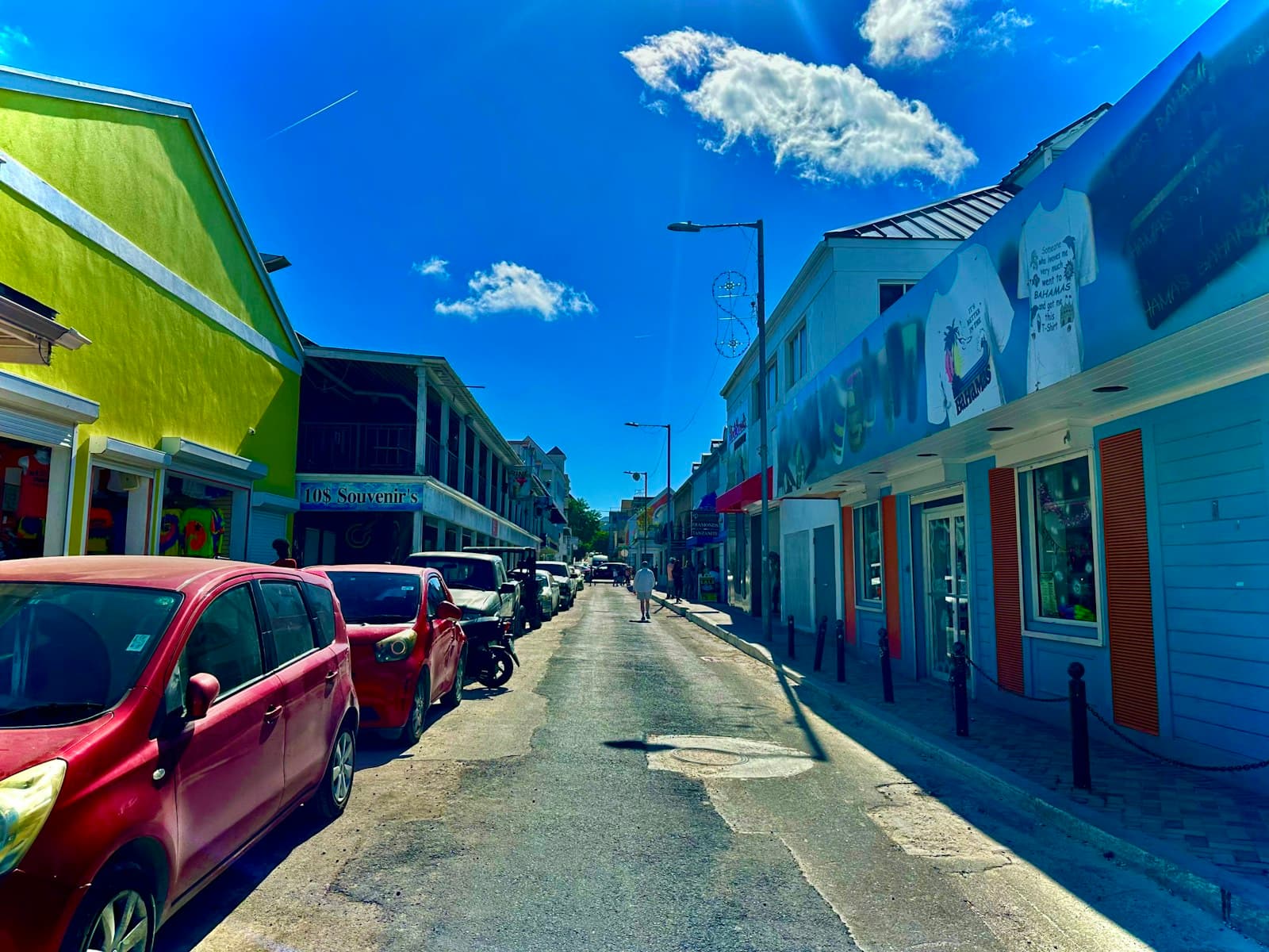 A sunny downtown Nassau street lined with painted shops and parked cars