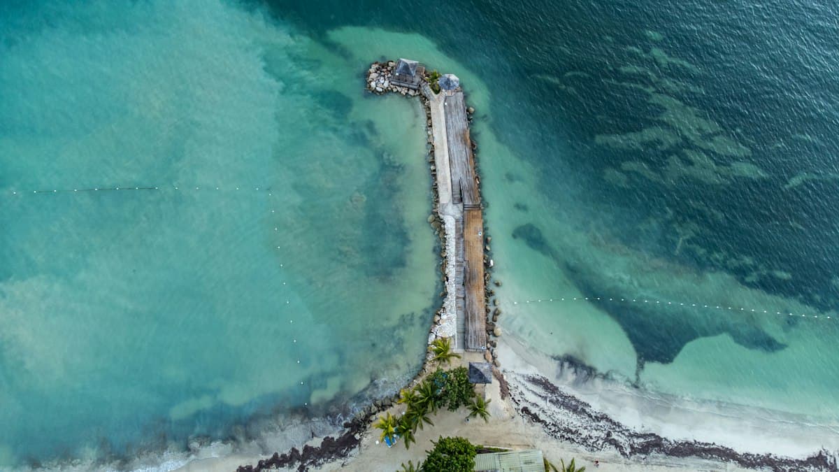 Aerial view of a wooden jetty reaching into turquoise water off a Jamaican beach