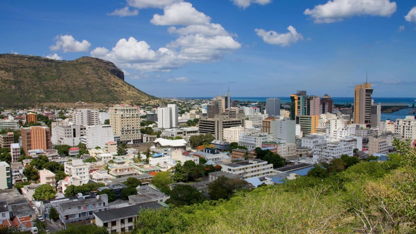Port Louis skyline with mid-rise buildings and green hills under a blue sky