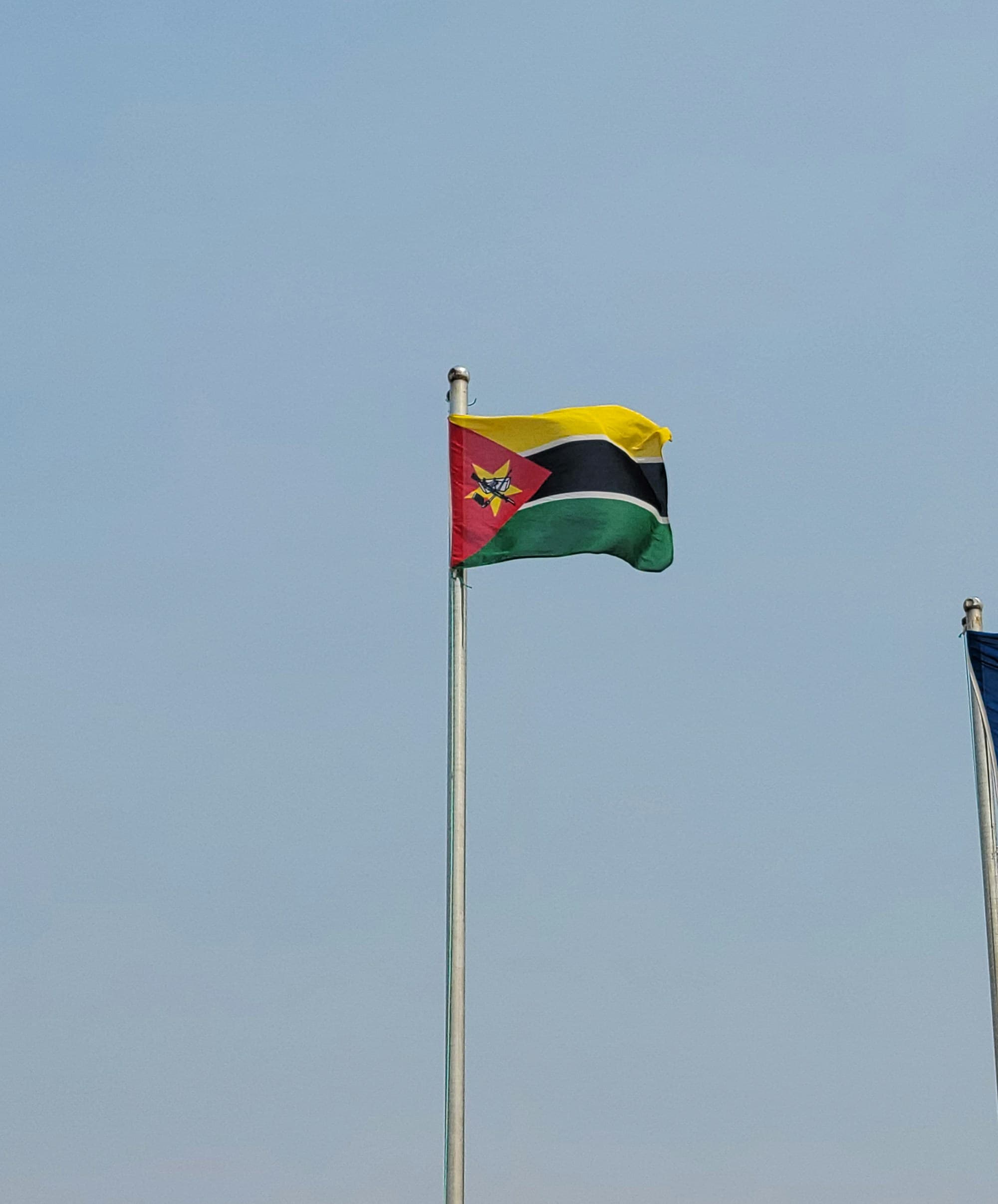 The flag of Mozambique flying on a pole against a pale blue sky