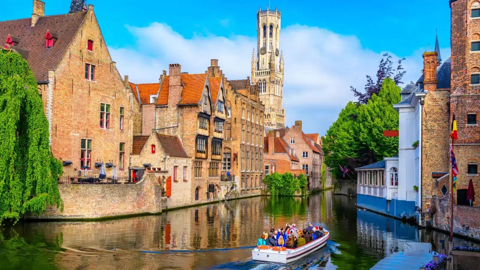 Brick houses and a belfry tower along a canal in Bruges on a sunny day