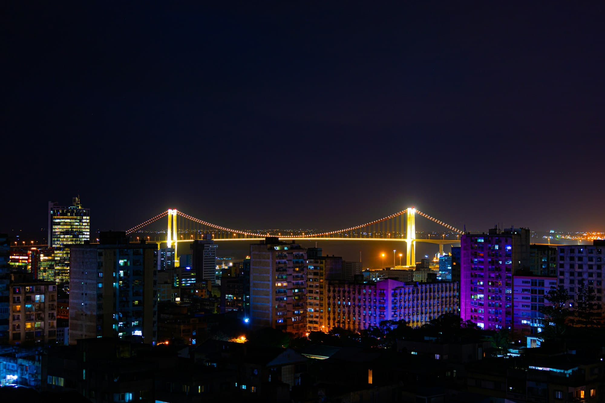 Maputo at night, with the lit suspension bridge over the bay behind the city's apartment blocks