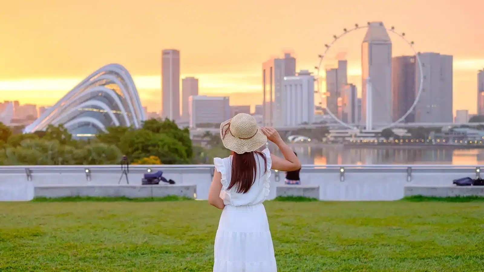 A woman in a sun hat looks across Marina Bay toward the Singapore Flyer at sunset