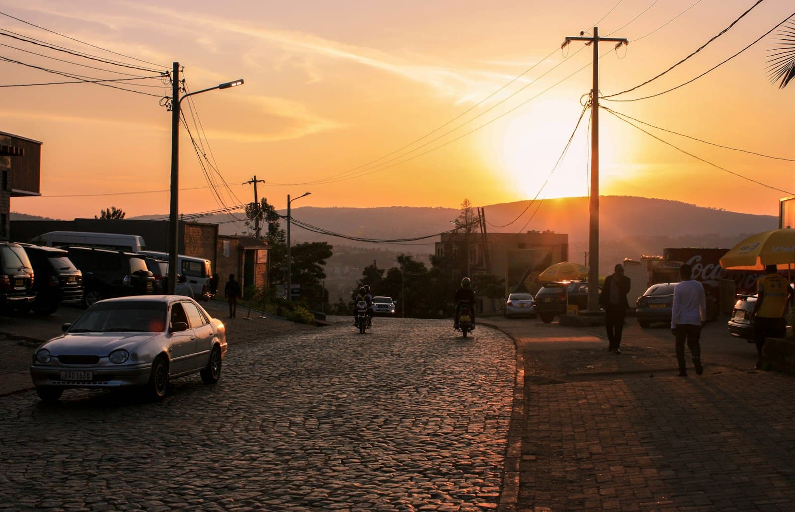 A cobblestone street in Kigali at sunset with motorbikes and hills in the distance