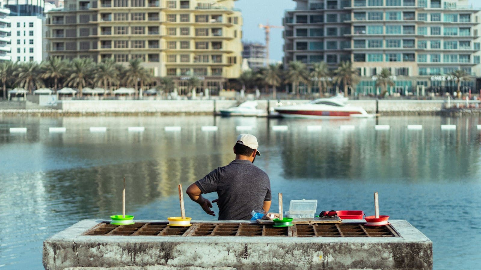 A man tending fishing lines on a seawall in front of waterfront apartment buildings in Bahrain
