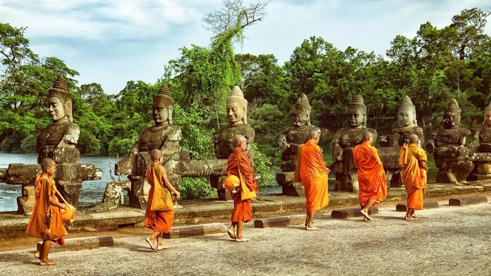 Monks walking past stone statues at a gate near Angkor, Siem Reap