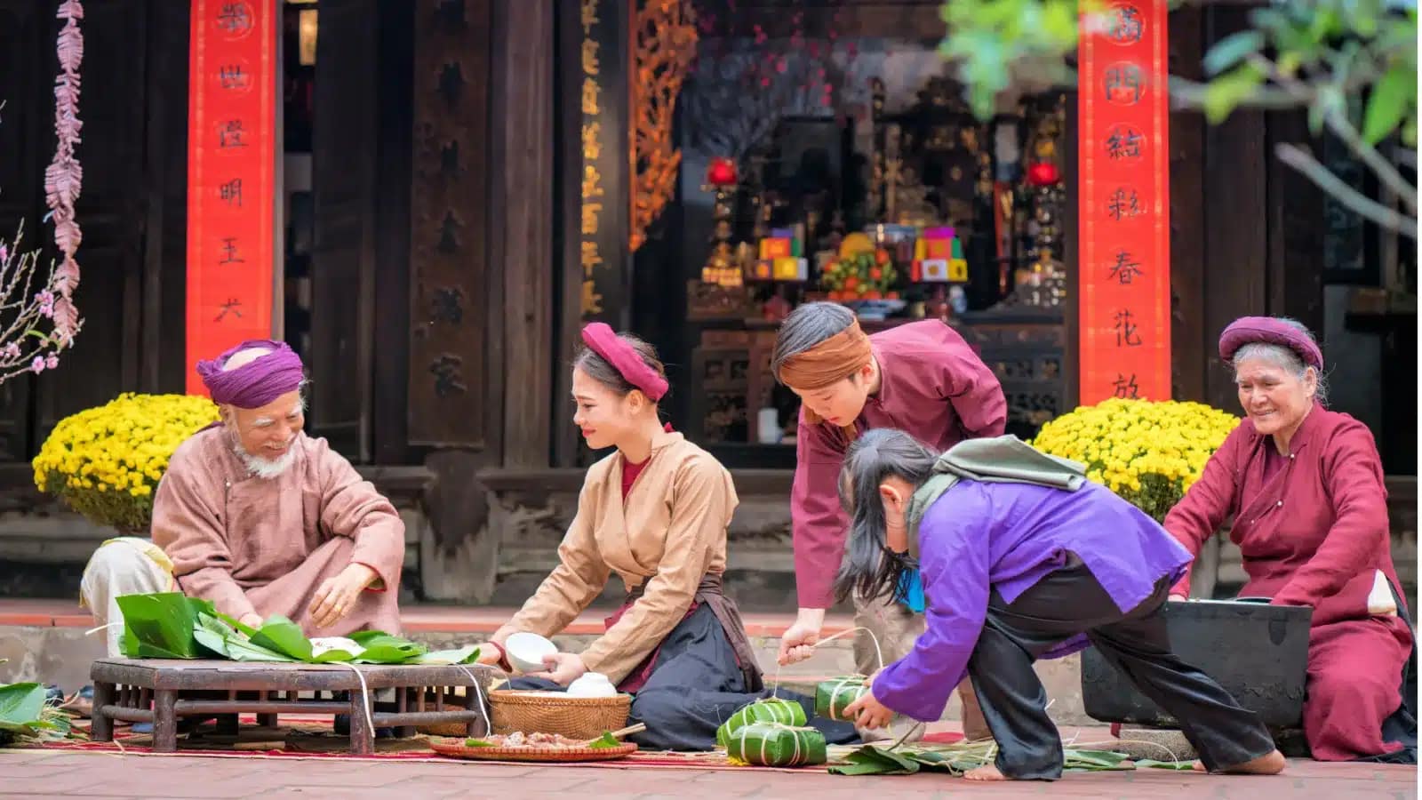 A Vietnamese family in traditional clothes wrapping bánh chưng rice cakes for Tết outside a temple