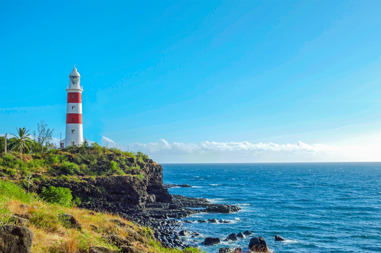 A red and white striped lighthouse on a rocky headland above the Indian Ocean in Mauritius