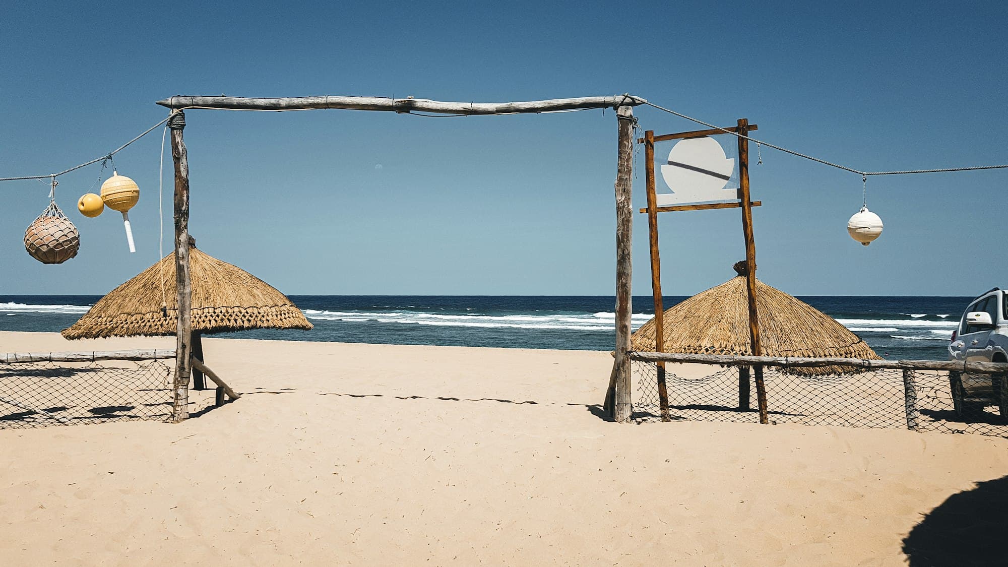 Thatched beach umbrellas and a driftwood gate on a sandy Mozambican beach facing the ocean