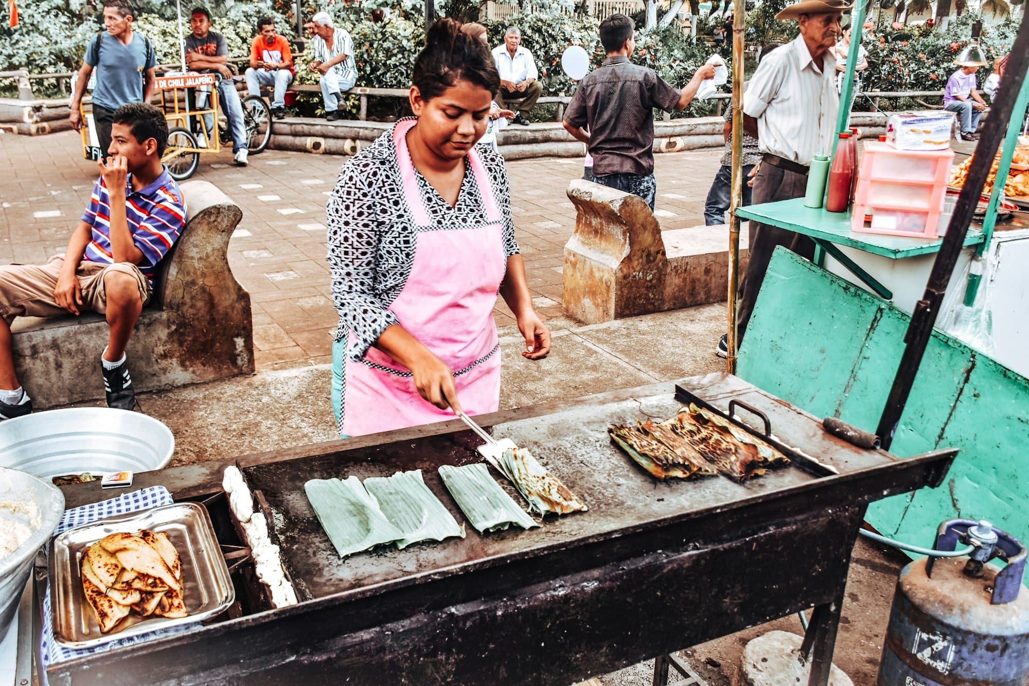 A cook grilling food wrapped in leaves at a street stall in a Salvadoran town plaza