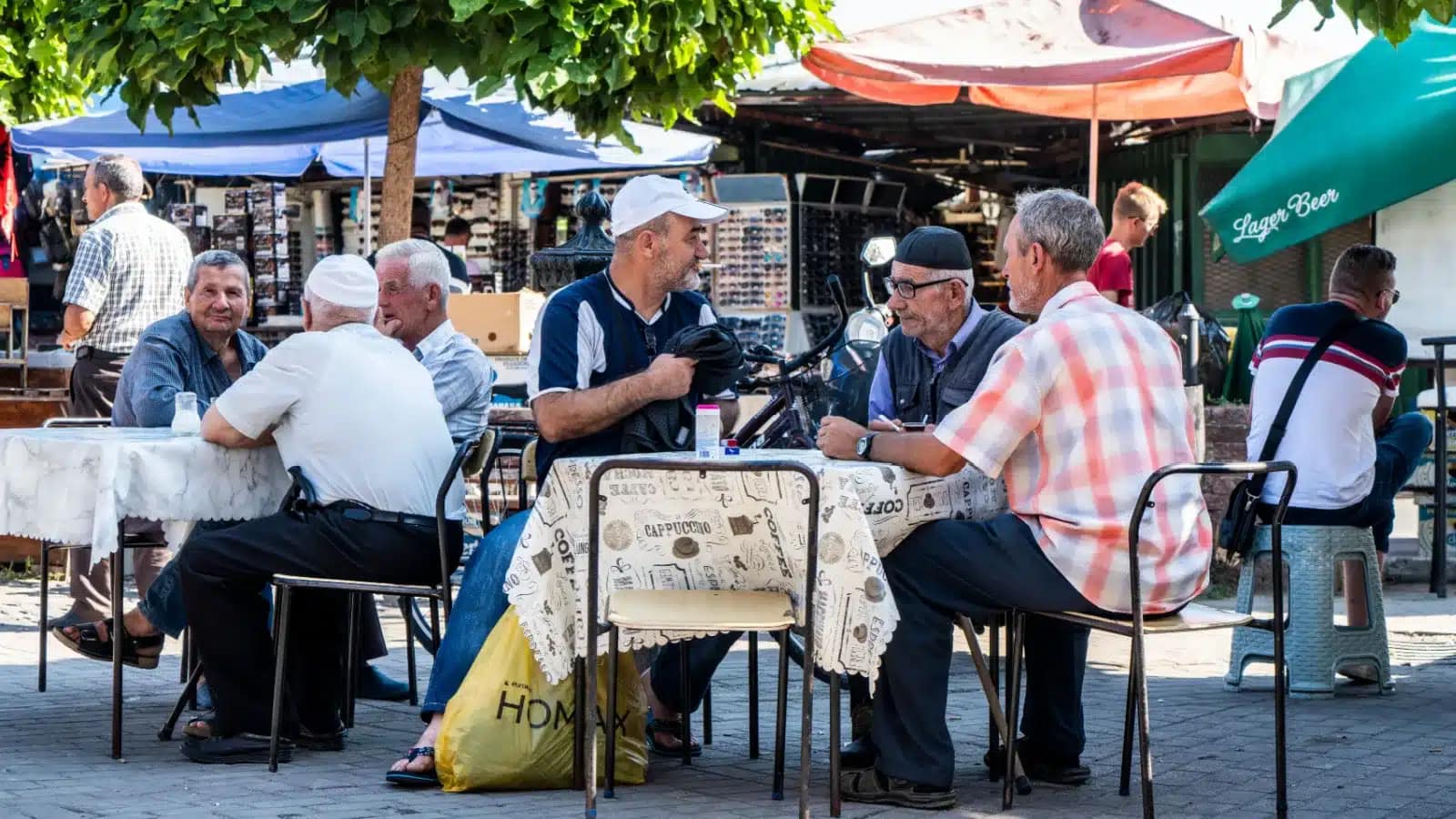 Older men talking at café tables under market umbrellas in North Macedonia