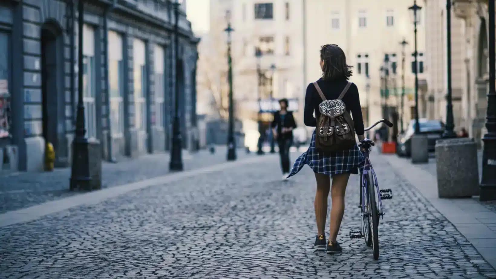 A woman walking her bicycle down a cobblestone street in Bucharest