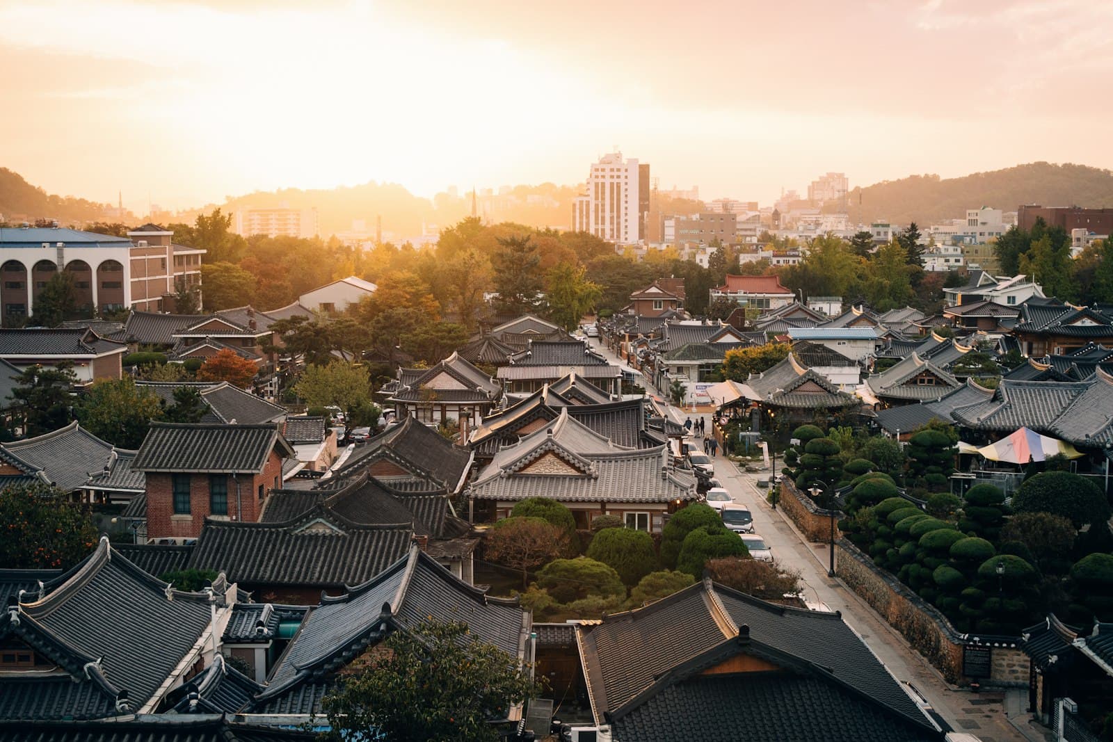 Tiled hanok roofs of Jeonju's traditional village glowing at sunset with the modern city behind