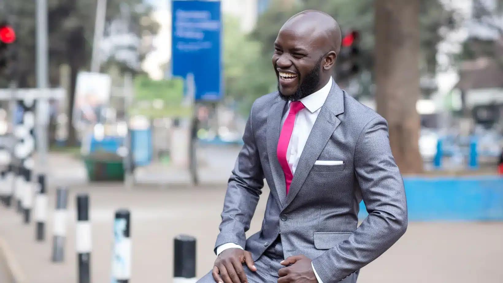 A smiling Kenyan professional in a gray suit on a Nairobi street
