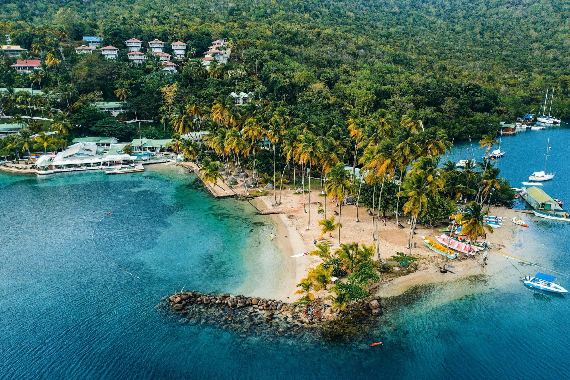 Aerial view of Marigot Bay in Saint Lucia with palm trees, a small beach, and sailboats at anchor