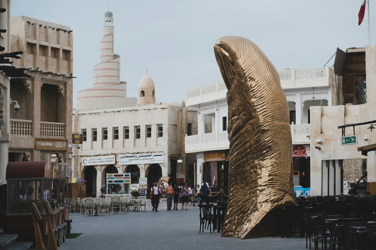 Shoppers walking through Souq Waqif in Doha past a giant bronze thumb sculpture