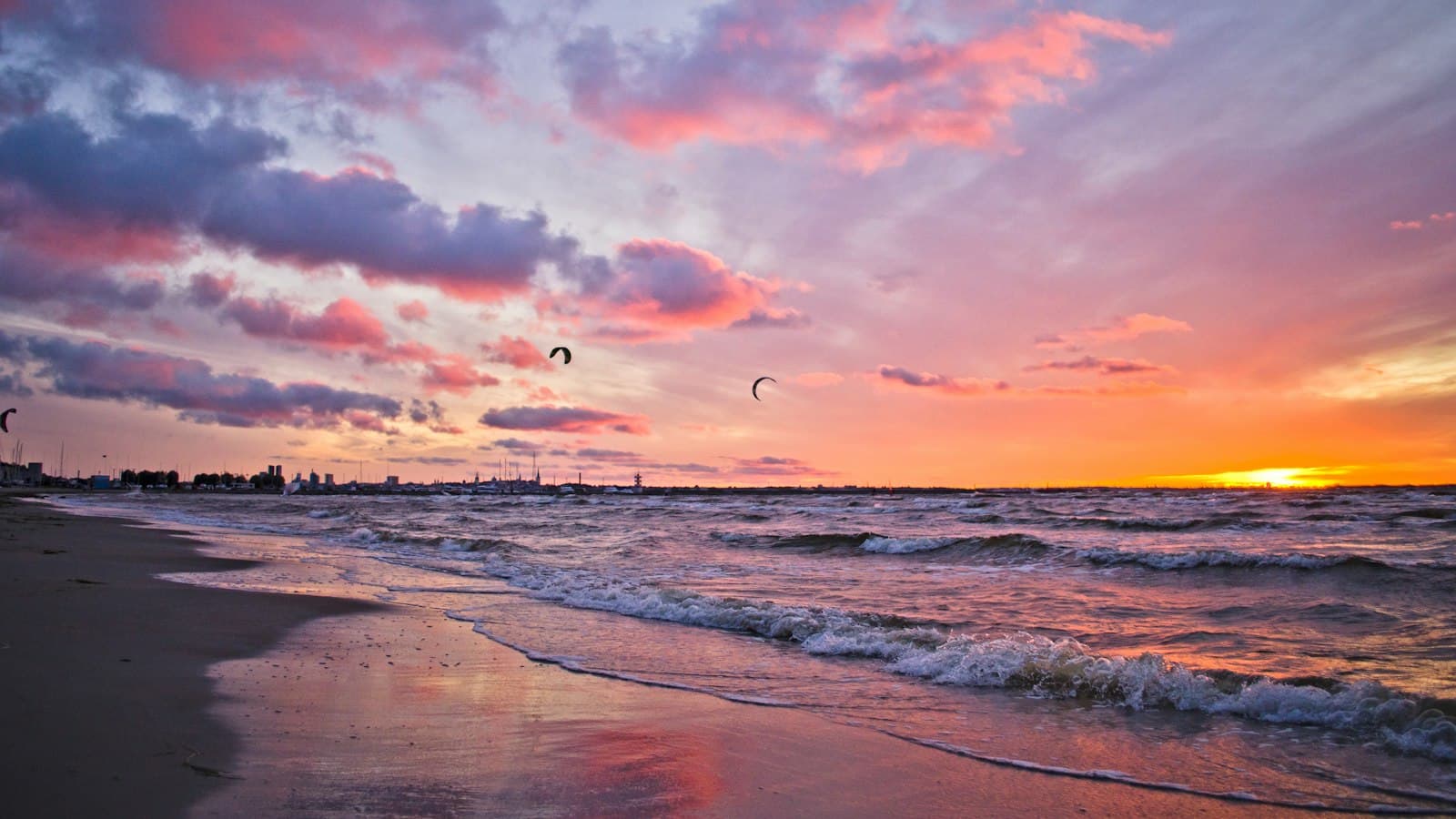 Kitesurfers ride a pink and orange sunset over a Baltic beach