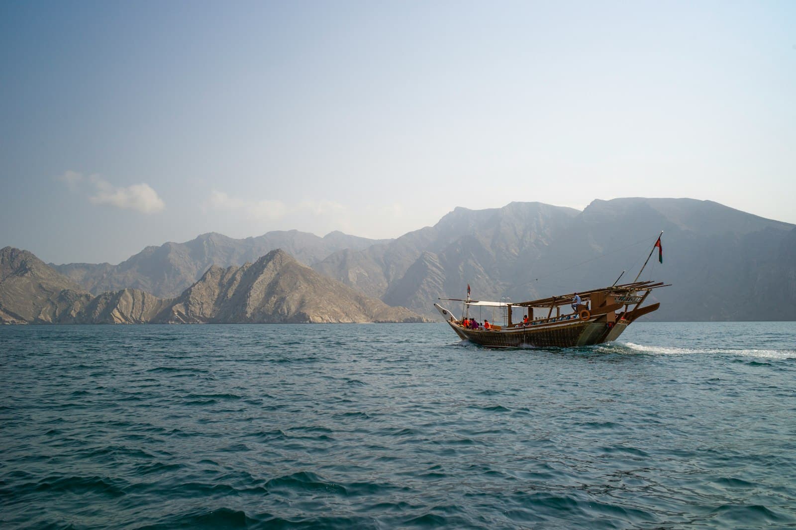 Traditional wooden dhow sailing past mountains in Musandam, Oman