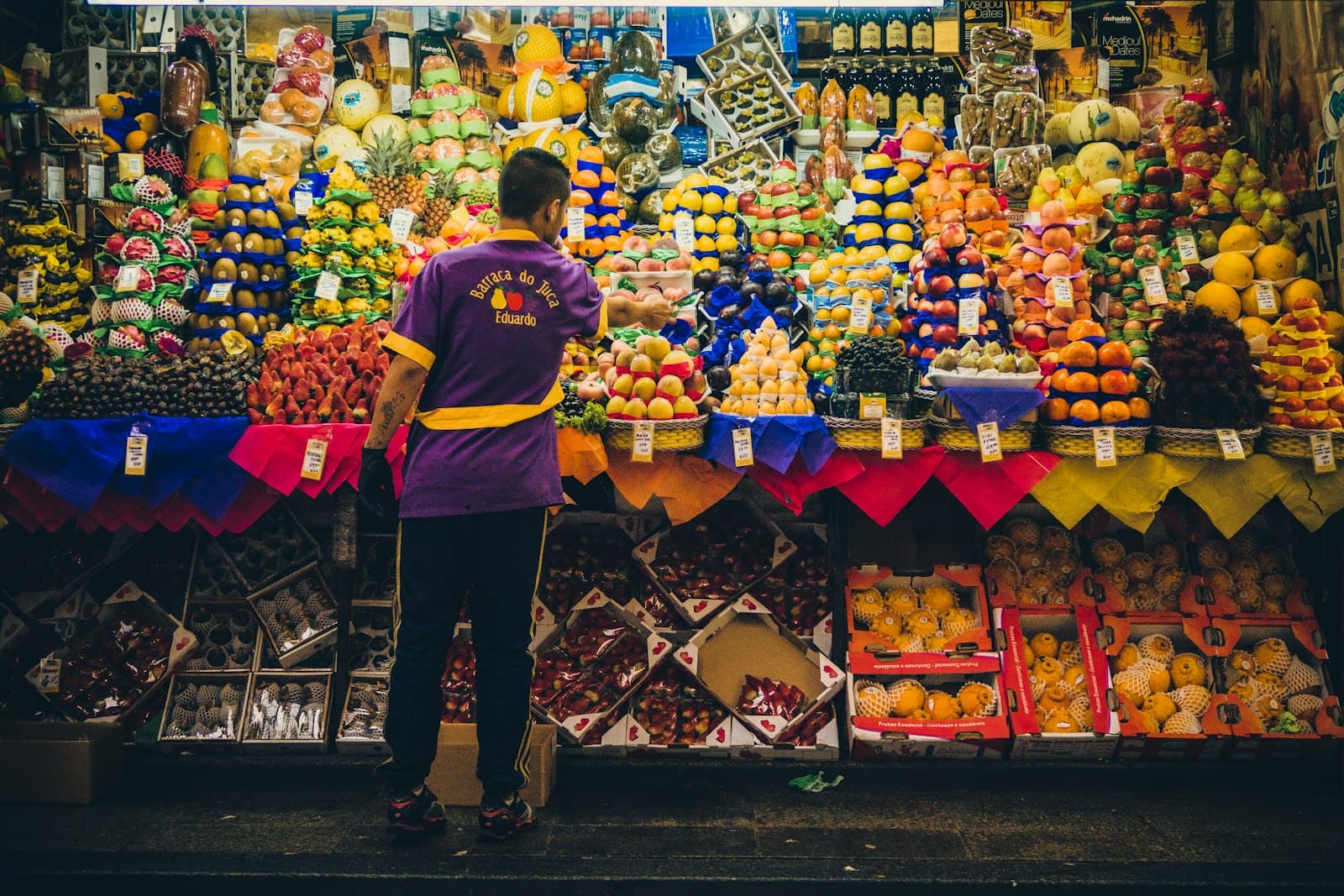 A vendor arranging tropical fruit at a busy produce stall in a Brazilian market hall