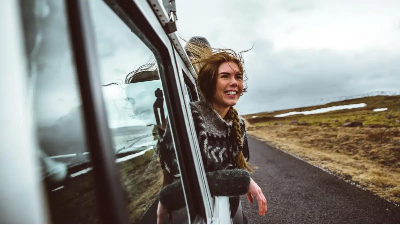 Smiling woman leaning out of a car window on a road through the Icelandic highlands