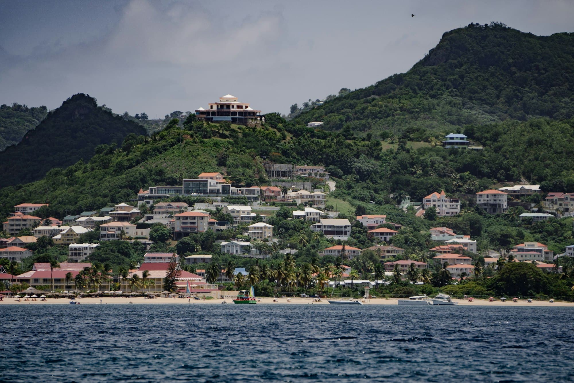 Villas and homes spread across a green hillside above a sandy beach on Saint Lucia's northwest coast
