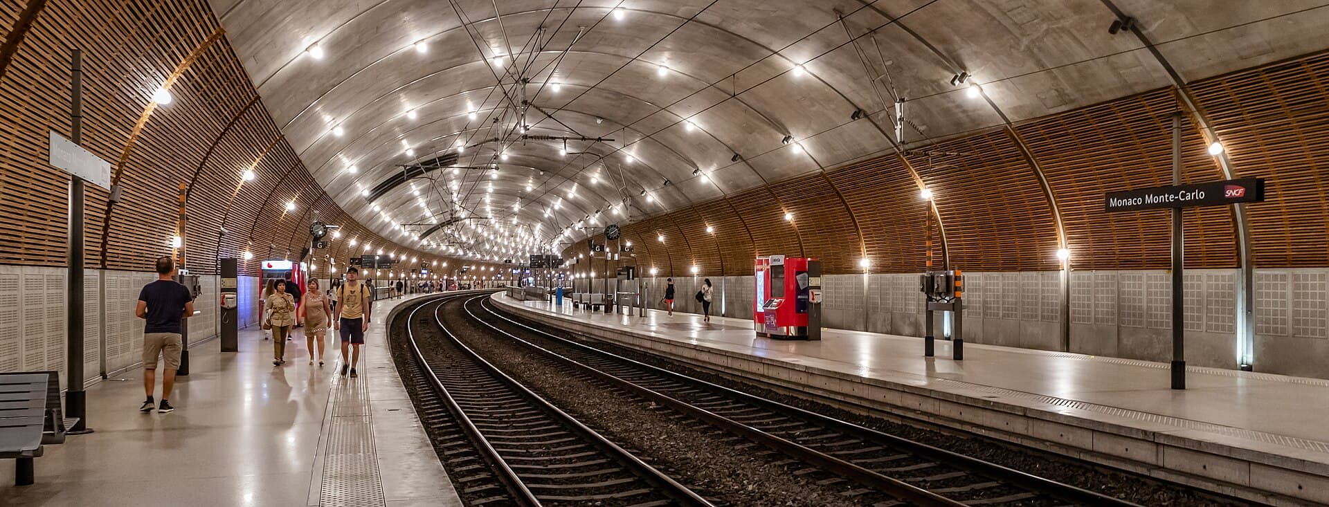 Commuters walking along the curved underground platform of Monaco Monte-Carlo train station