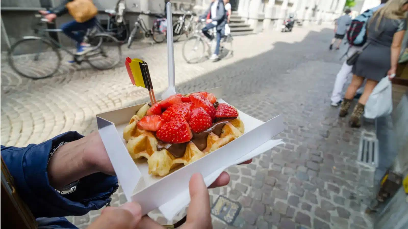 A Belgian waffle with strawberries and chocolate held up on a cobblestone street