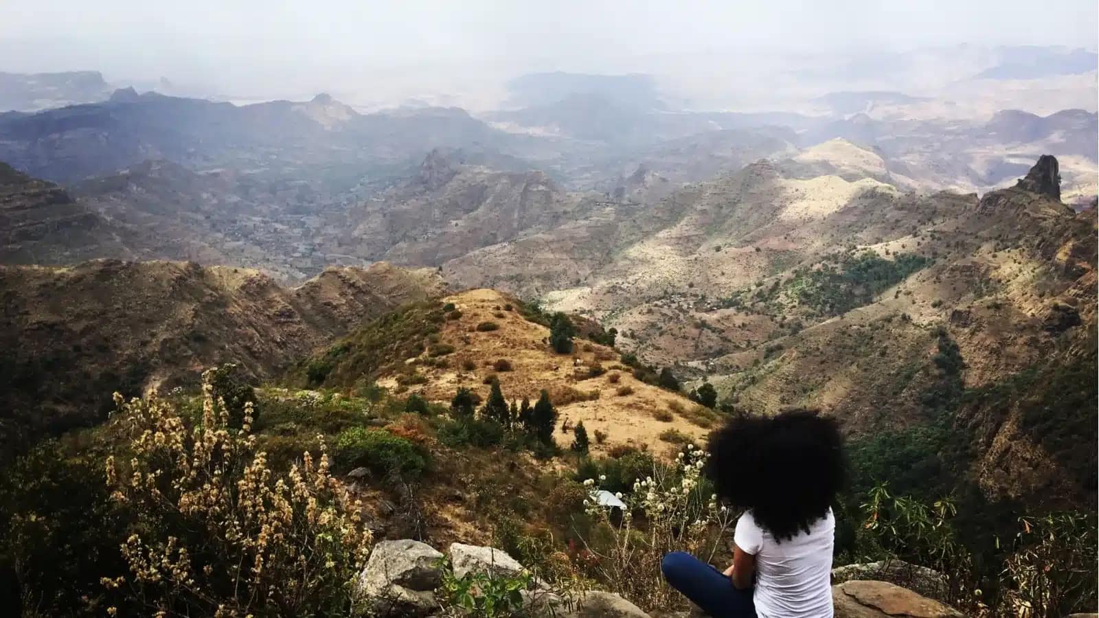 A student sits on a ridge looking out over the rugged Ethiopian highlands