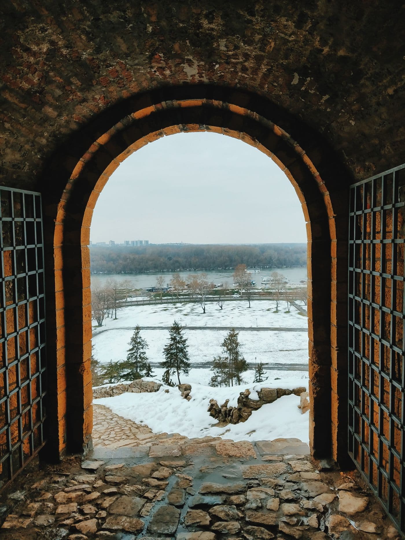 View through a brick archway at Belgrade's Kalemegdan Fortress toward the snowy riverbank