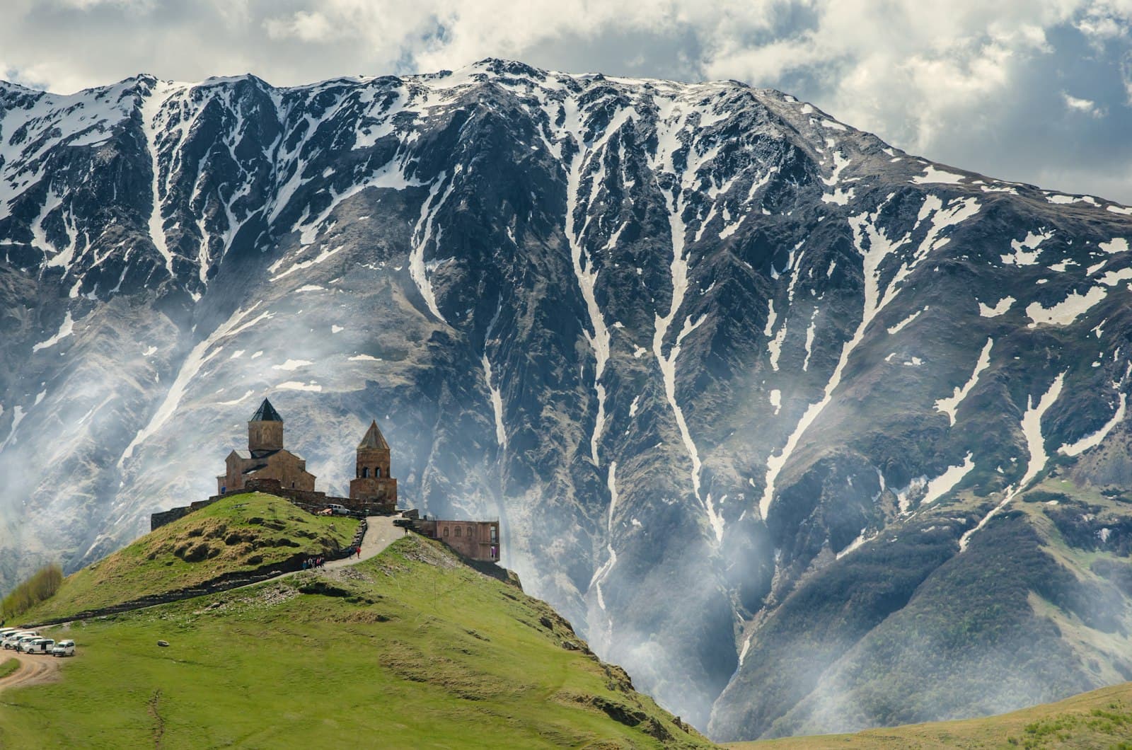 Gergeti Trinity Church on a green hilltop below snow-streaked Caucasus peaks