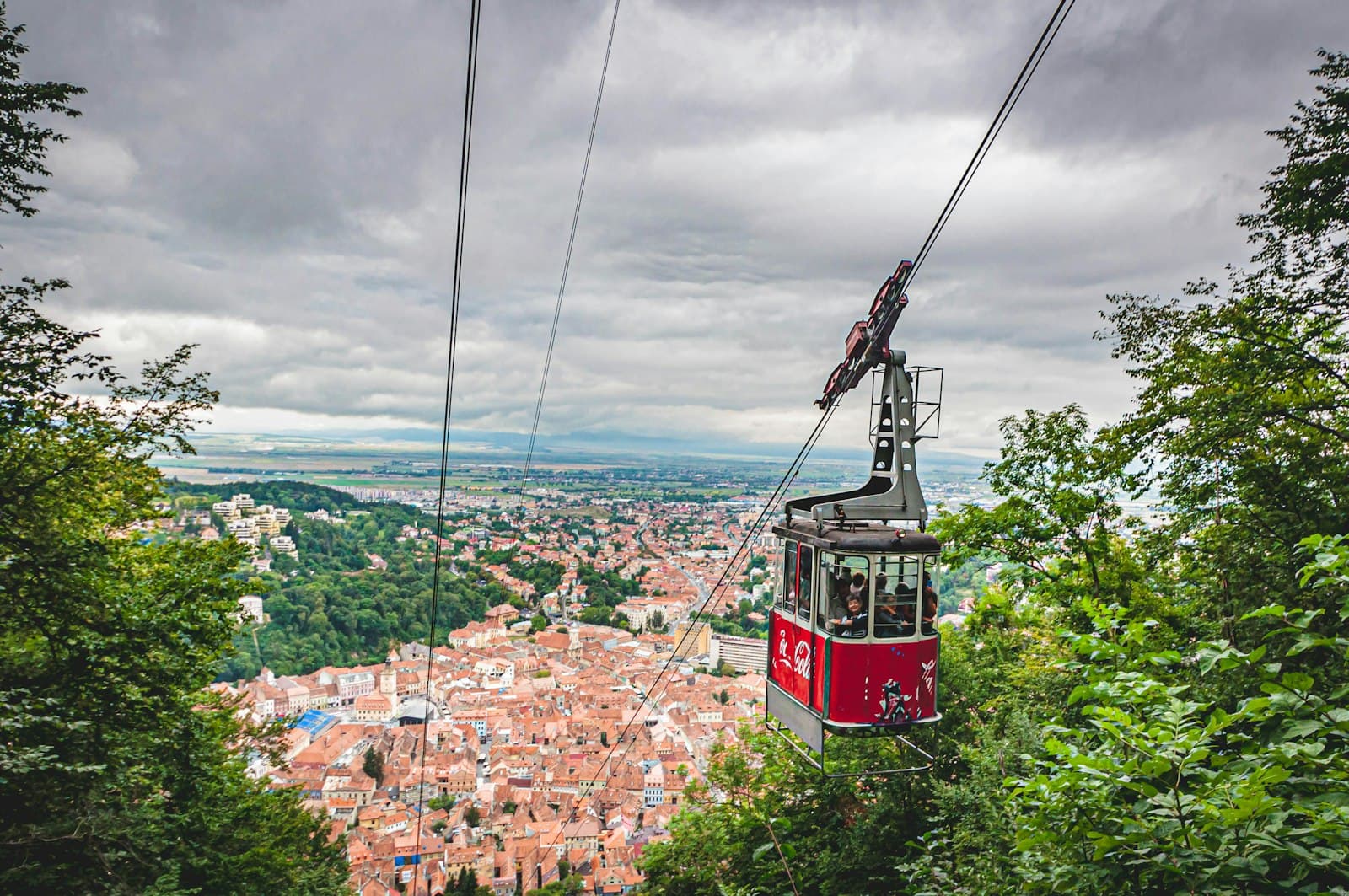 Red cable car climbing above the terracotta rooftops of Brașov