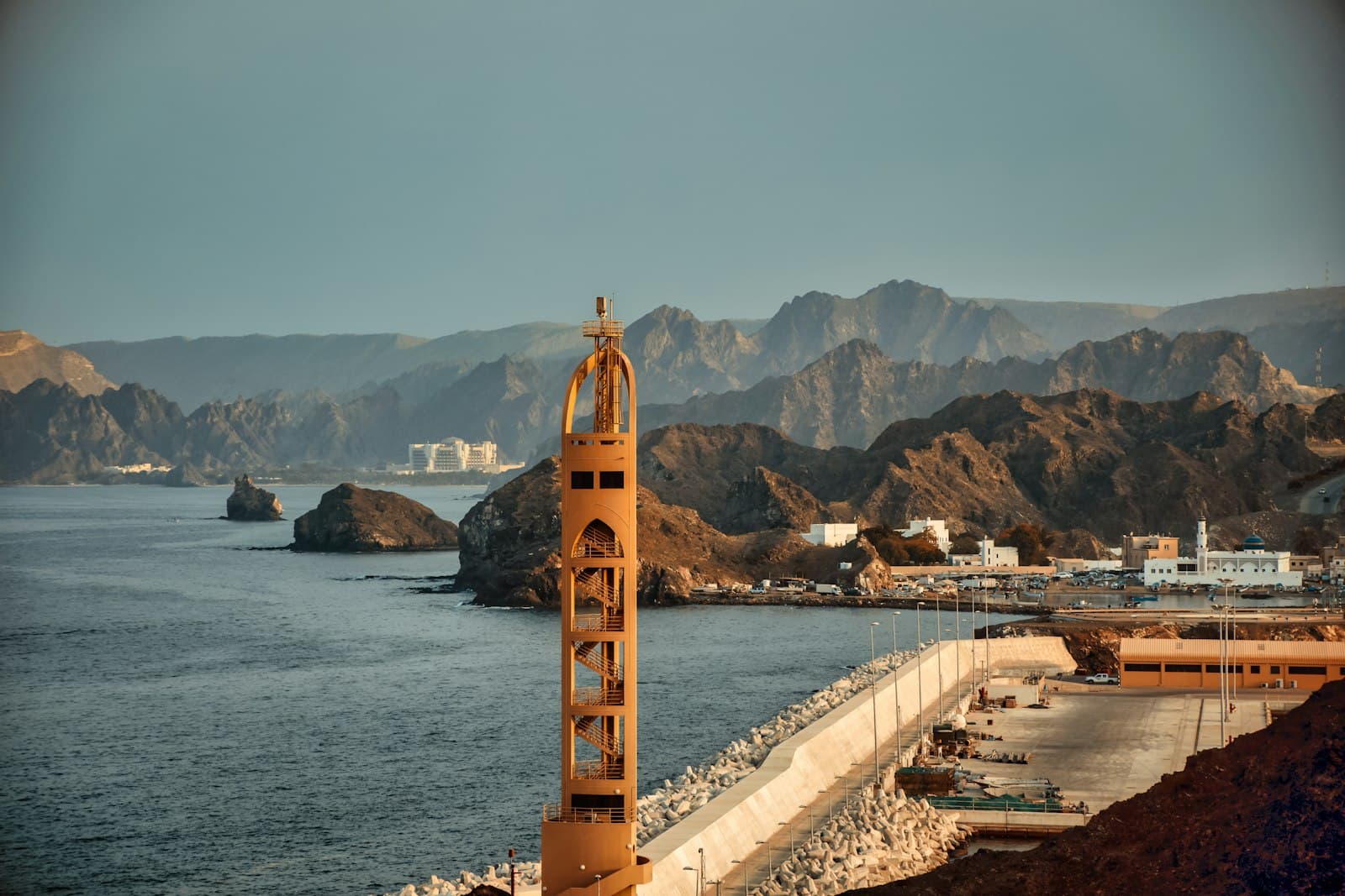 Harbor tower and rocky coastline in Muscat with the Hajar Mountains behind