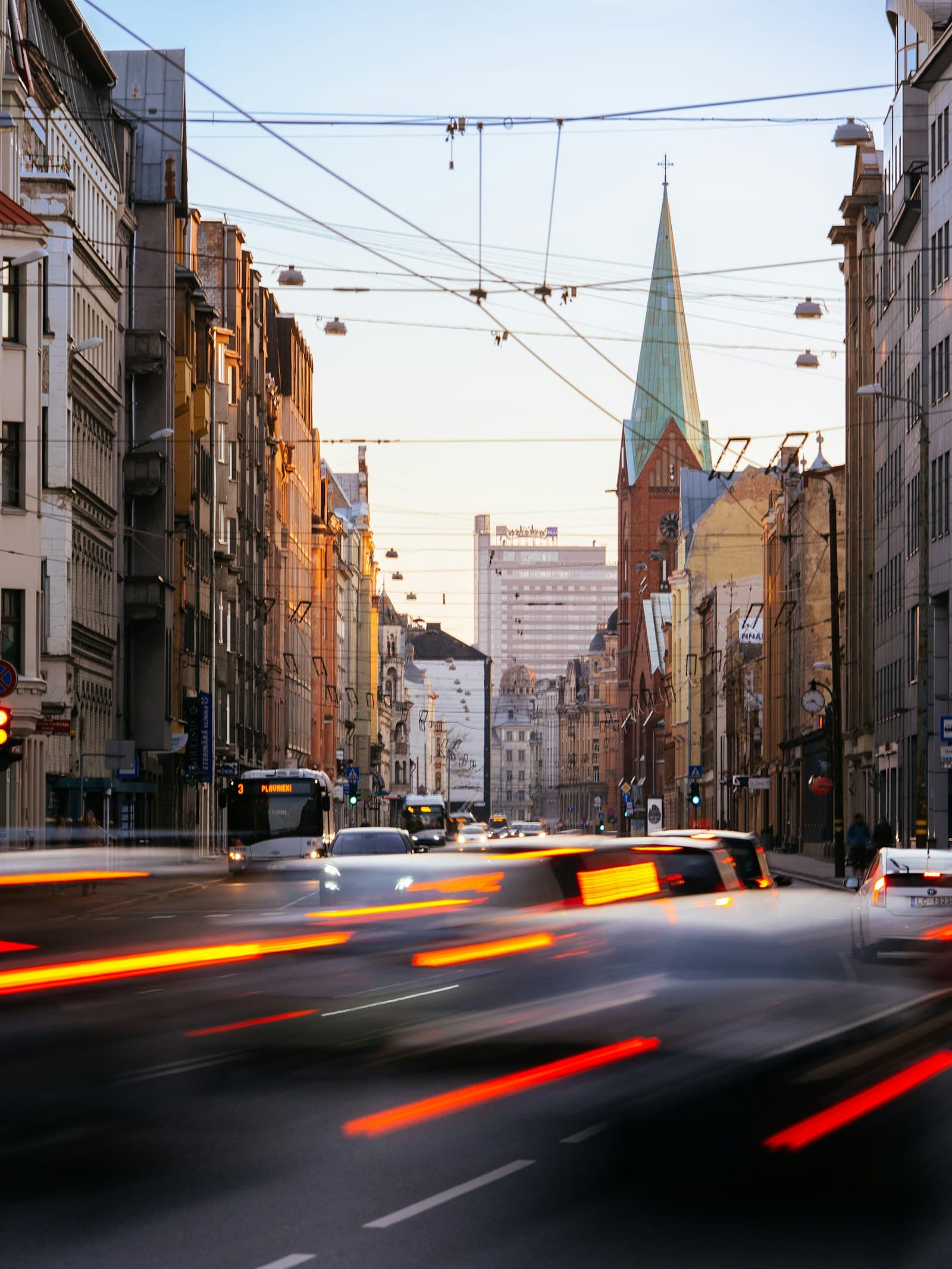 Evening traffic on a Riga street lined with old apartment buildings and a green church spire
