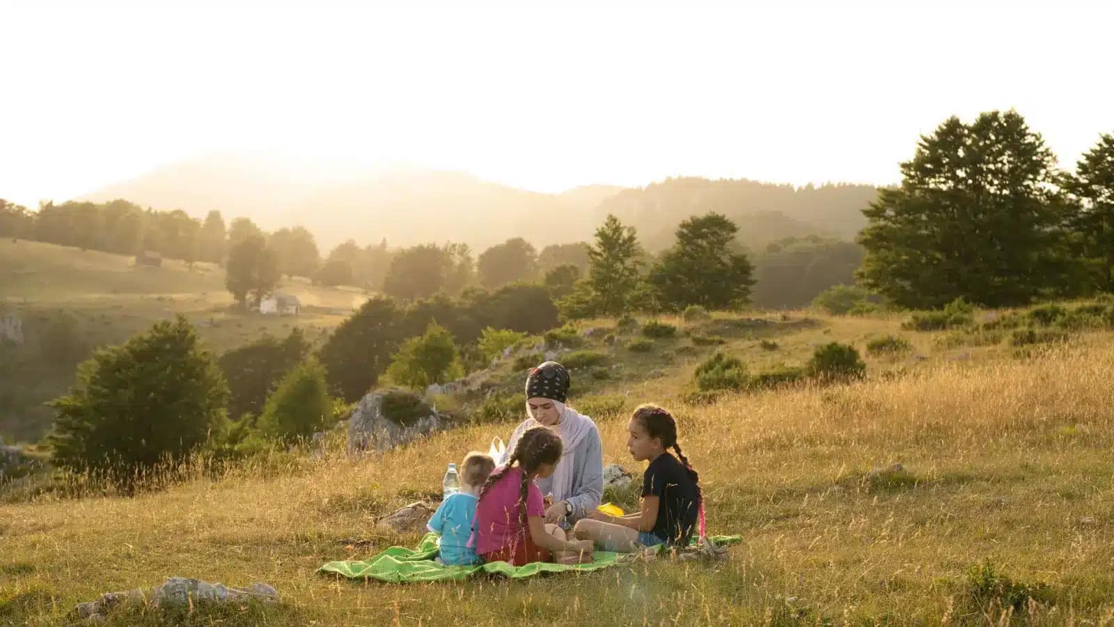 A family picnicking on a hillside meadow at sunset in Bosnia and Herzegovina