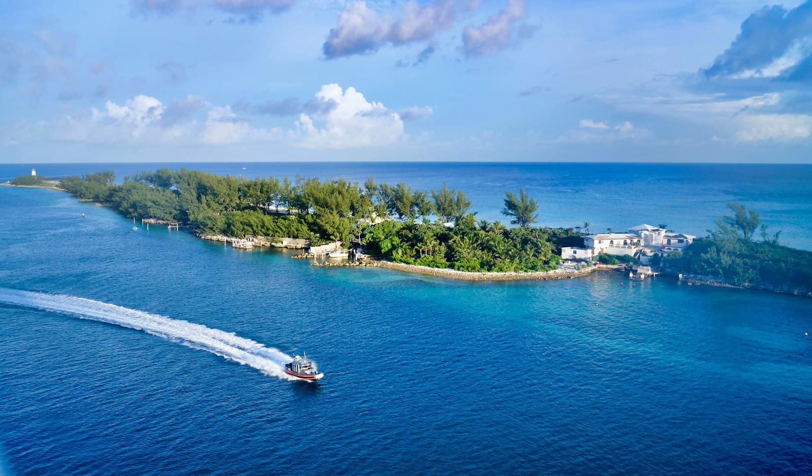 A boat speeding past a green point of land at the entrance to Nassau harbor
