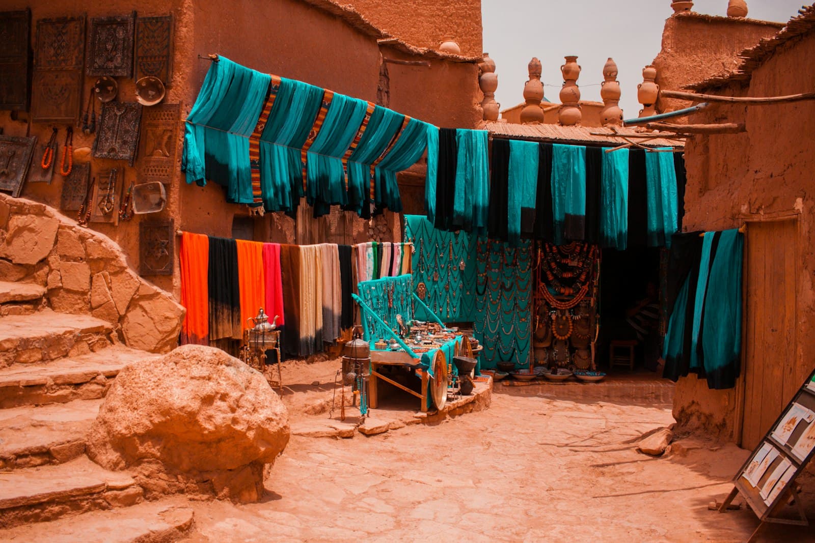 Teal and orange scarves hanging over a sandy lane in a southern Moroccan kasbah