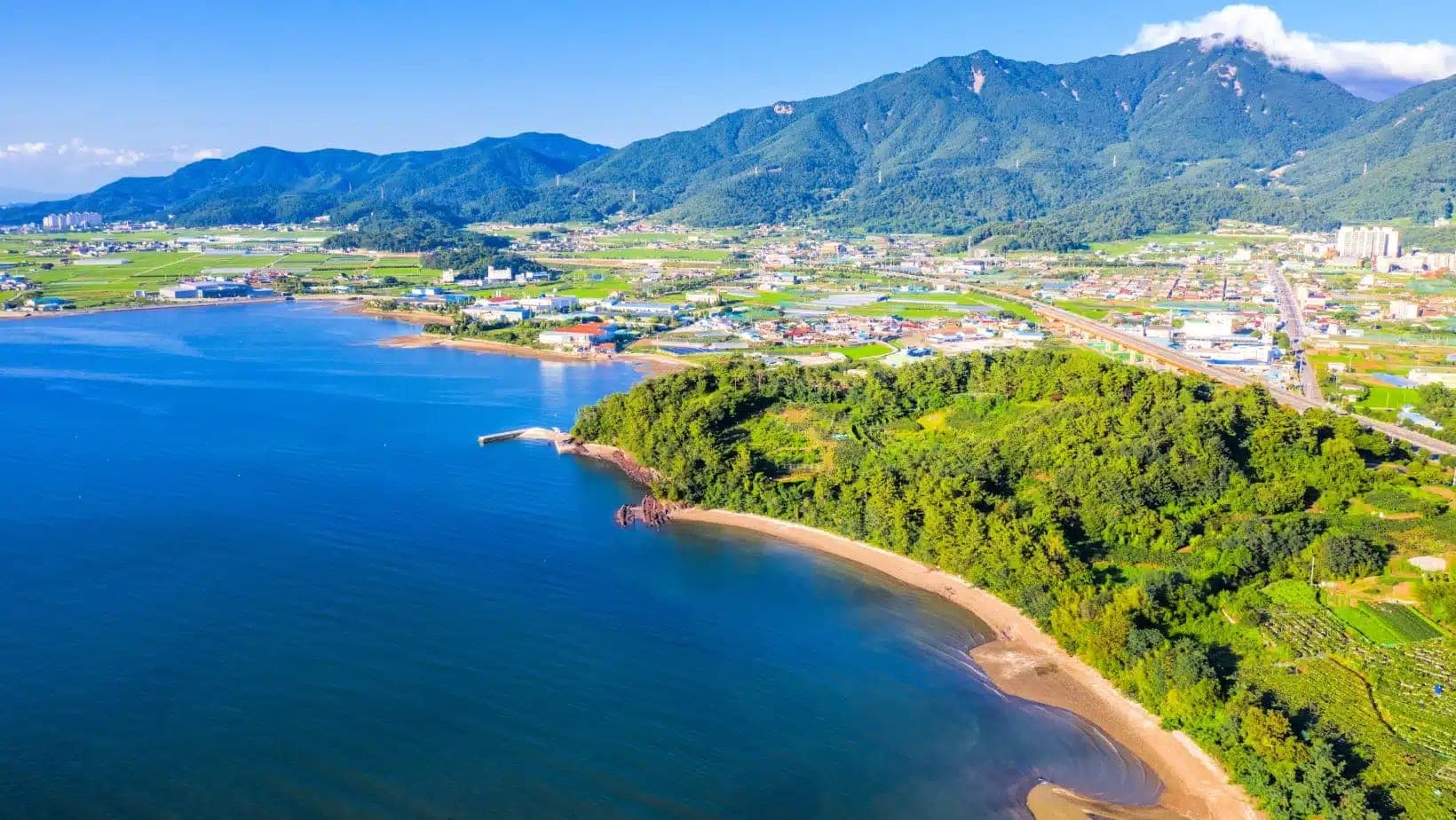Green hills and farmland meeting a blue bay on the coast of Sacheon, South Korea