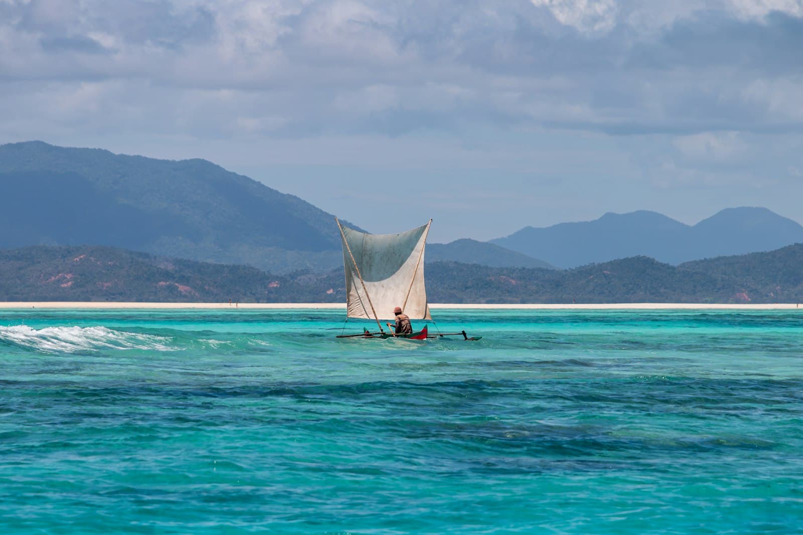 A fisherman sails a traditional outrigger pirogue across turquoise water off the coast of northern Madagascar